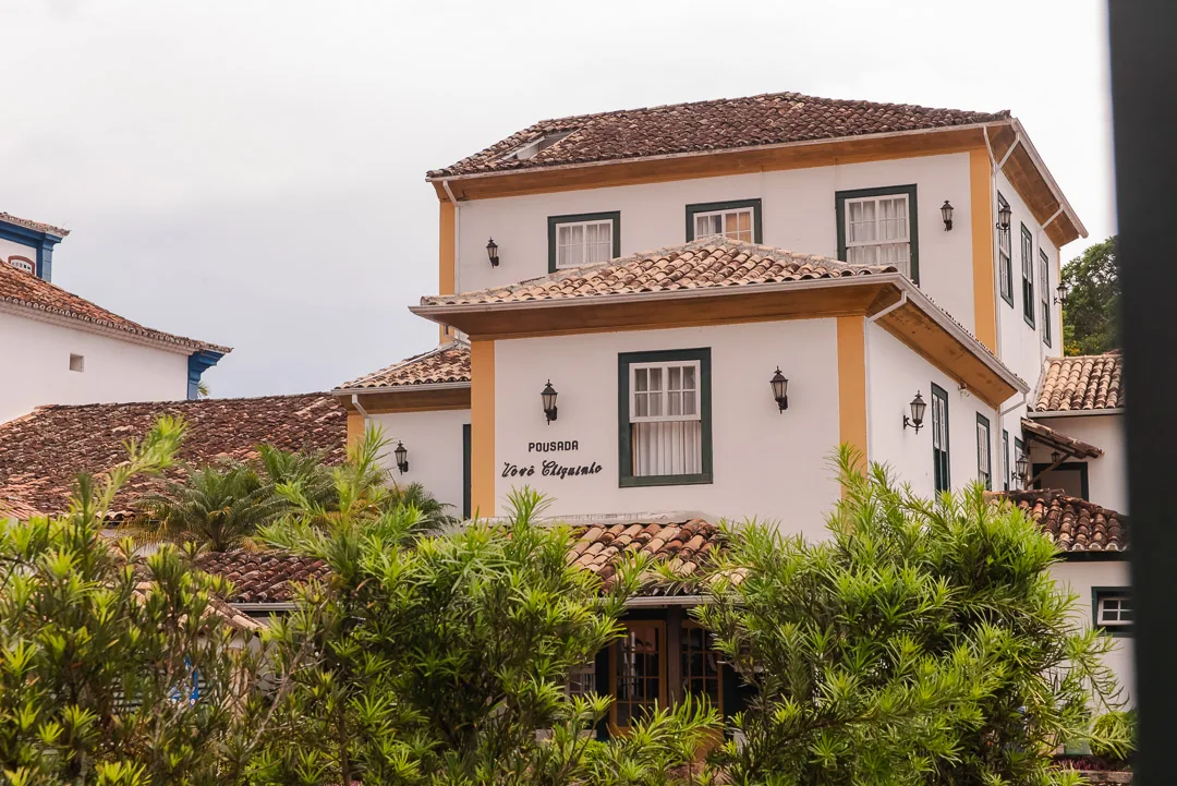 Fachada colonial da Pousada Vovô Chiquinho, com telhados de telha, janelas de madeira e jardim na frente